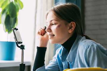 A teenage girl shows how to dye her eyebrows and eyelashes while recording a video for her blog on...