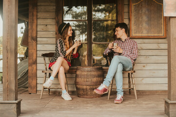 Couple drinking tea / coffee in the Wild West, in Western house. Girl in hat with long hair. Girl and boy smile, laughing. Incredible trip, travelers. Sit on the terrace.  Conceptual place