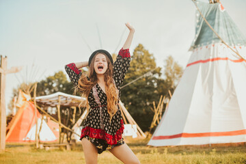 Young beautiful girl smiling on background teepee, tipi- native indian house. Pretty girl in hat...