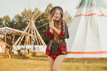 Young girl beautiful tourist talking on the phone, video communication roaming on the background teepee / tipi- native indian house. Unusual places to stay © MoreThanProd