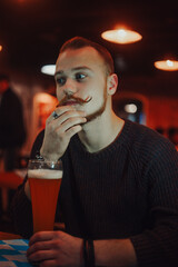 A man in a bar drinks beer, a handsome red-haired guy with a long mustache in a pub.
