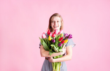 Happy young woman holding bouquet of fresh tulips isolated on pink background
