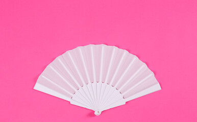 White hand fan on pink background, top view
