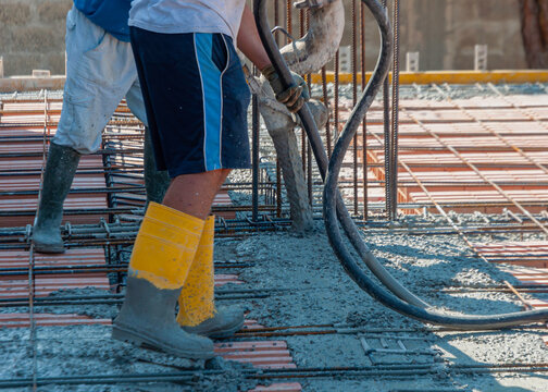 Building construction worker pouring cement or concrete with pump tube. Details of worker and machinery