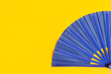 Blue hand fan on yellow background, top view. Space for text