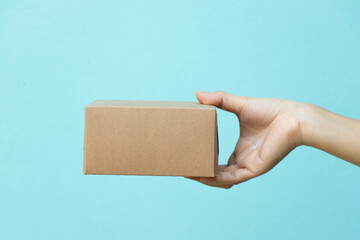 Woman hand hold the brown corrugated box on blue wall background with copy space