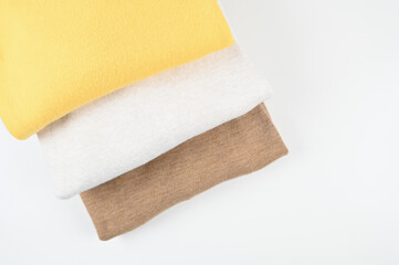Top view of folded beige, brown, mustard knitted pullovers isolated on white. Simple minimal cozy clothes concept.