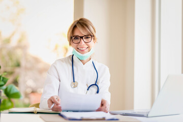 Shot of female doctor wearing face mask while sitting at desk in doctor's office and working