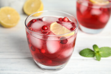 Tasty refreshing cranberry cocktail with lemon on white wooden table, closeup