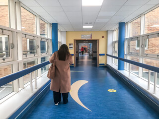 A woman walks down a hospital corridor which is long and striight.