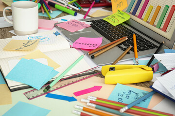 Laptop, notes and office stationery in mess on desk. Overwhelmed with work