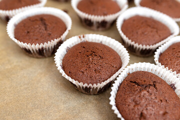 Brown chocolate muffins wrapped in white paper baked in the oven, lying on baking paper.
