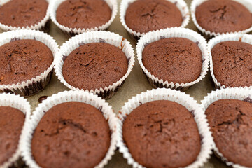 Brown chocolate muffins wrapped in white paper baked in the oven, lying on baking paper.