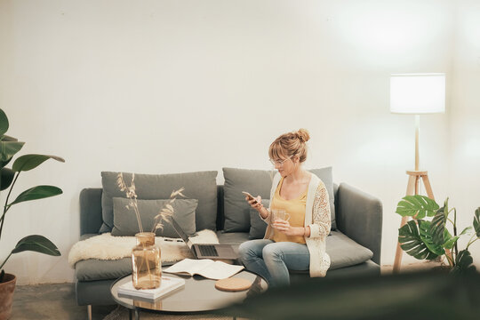 Millennial Woman Working From Home Checking Email On A Smartphone And Drinking Tea, Wide Shot