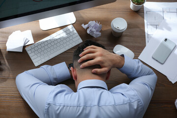 Stressed out businessman at workplace in office, top view