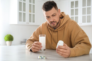 Man taking medicine for hangover at table in kitchen