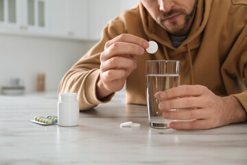 Man taking medicine for hangover at table in kitchen, closeup