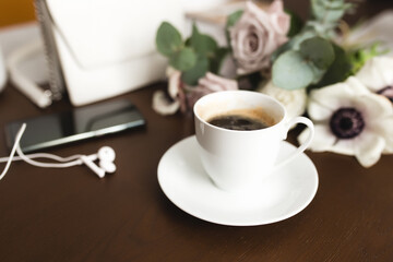 Cup of coffee, bouquet of anemone, purple roses, woman handbag, phone on table