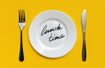 A white plate on which the word Lunch time is written standing on a yellow tablecloth . The concept of a balanced diet, ration and medical fasting. Top view, background, copy space.