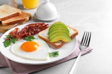 Romantic breakfast with fried bacon, heart shaped egg and avocado toast on light grey table. Valentine's day celebration