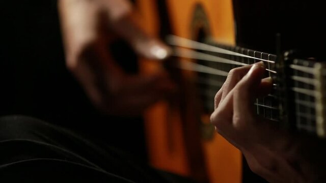 closeup of hands playing a classical wooden guitar with black background, left hand on focus and right hand out of focus in a beautiful bokeh