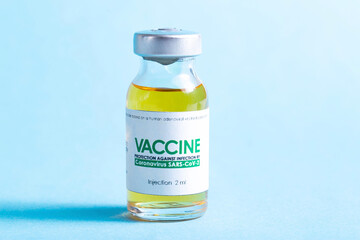 Vial with coronavirus vaccine on blue background, close-up. Vaccination of the population against coronavirus, SARS-Cov-2