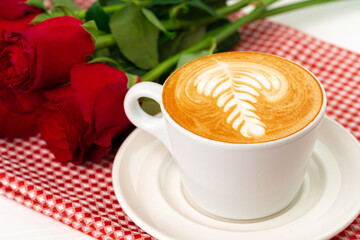 Cup of cappucino with art and bouquet of roses on wooden table