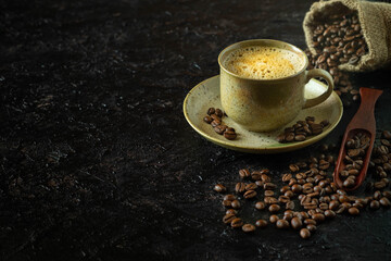 Hot coffee cappuccino or latte with milk foam for morning menu in vintage brown ceramic cup with coffee beans roasted in burlap sack bag on dark grunge table background. Flat lay with copy space.