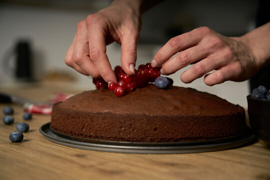 Woman with a passion for cooking decorates a homemade chocolate cake in her home kitchen with blackberries and red currants.