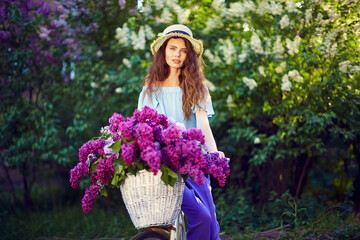 Portrait of a happy beautiful young girl with vintage bicycle and flowers on city background in the sunlight outdoor. Bike with basket full of flowers. Active Leisure Concept.