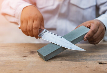 A man sharpens a knife hiking with a whetstone.