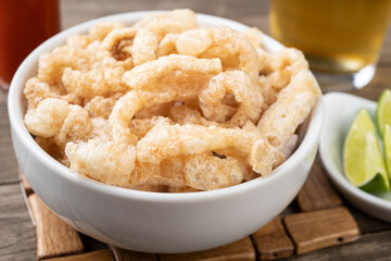 Fried pork cracklings on a white bowl with lemon and beer over wooden table