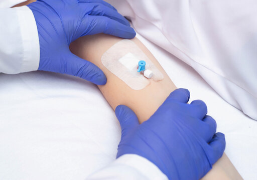 A doctor in medical gloves holds the patient's hand with an intravenous catheter. Concept of human blood diseases, leukemia, copy space for text