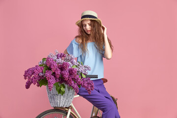 Portrait of a happy beautiful young girl with vintage bicycle and flowers on pink background. Bike with basket full of flowers. Active Leisure Concept.