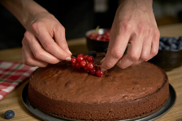 Woman with a passion for cooking decorates a homemade chocolate cake in her home kitchen with blackberries and red currants.