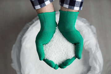 Farmer holding pile of ammonium nitrate pellets over bag, top view. Mineral fertilizer