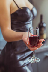 slim woman in a leather dress holds a wineglass with red wine 