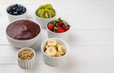 Brazilian typical acai bowl with fruits and muesli over wooden background with copy space