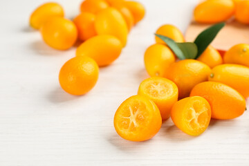 Fresh ripe kumquats with green leaves on white wooden table