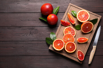 Whole and cut red oranges on wooden table, flat lay. Space for text