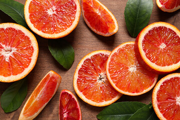 Slices of fresh ripe red oranges and green leaves on wooden table, flat lay