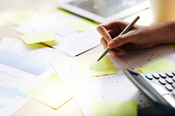 Hands of entrepreneur writing ideas on yellow stickers when working with reports at office table