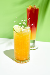 Mango lemonade drink over green background. White table with sunlight and palm leaf hard shadow. Summer, tropical and juicy concept