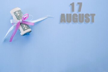 calendar date on blue background with rolled up dollar bills pinned by blue and pink ribbon with copy space. August 17 is the seventeenth day of the month