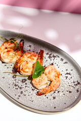 Restaurant seafood - Shrimp Grill Seafood Plate. Appetizer food plate on white table with pink wall. Day sunlight with hard shadow of monstera palm leaves. Summer or spring food concept.