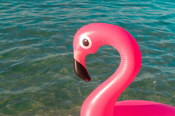 Summer fun. Pink inflatable flamingo in blue sea water on summer ocean beach background. Luxury...