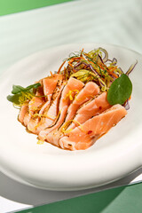 Salmon tataki in sesame with salad. Fish sashimi restaurant appetizer on white table with green wall. Day sunlight with hard shadow of tropical palm leaves. Summer or spring food concept.