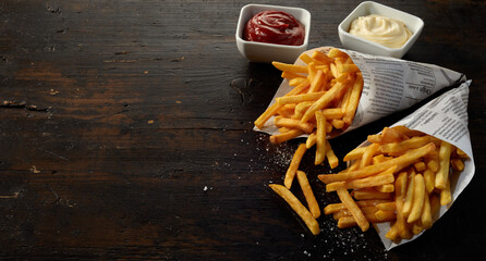 Tasty French fries in paper cones near sauces