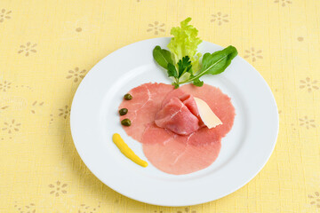 carpaccio on a white plate on a yellow tablecloth