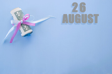 calendar date on blue background with rolled up dollar bills pinned by blue and pink ribbon with copy space. August 26 is the twenty-sixth day of the month